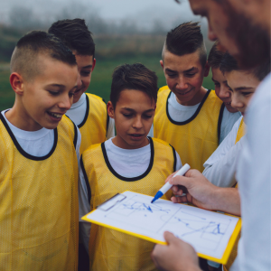 group of boys in yellow sports bibs listening to a coach giving instructions with a clipboard